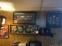 Photo showing three framed hockey memorabilia pieces mounted on a wood-paneled wall including a print and a shadow box with gloves and goalie mask.