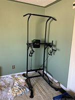 Front angle view of the Soozier exercise power tower showing padded handles, frame base and resistance cables, with cloth on floor.