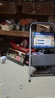 View showing folding step stool in front with wooden shelves holding trays of wire spools, connectors, and hardware supplies in background.