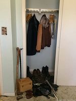 Photo of closet with hanging jackets and jackets and pants, shoes on floor, wooden shoe shine box, canes and ice grippers visible