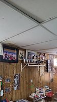 Wall with multiple framed John Wayne prints, collector's plates on shelf, and posters visible along wood panel walls.