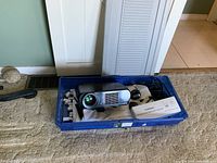 Orion projector and mounting bracket stored in blue plastic bin with white projection screen fabric inside.