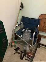 Full view of the lot items including walking poles, blue foldable lawn chair, racquets, small football, mosquito repellent sprays, axe, and multi-tool on beige carpet.