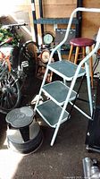 Photo showing white aluminum folding ladder with three steps and a round metal step stool beside it