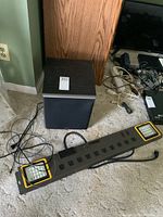 Prime power strip and Edifier subwoofer placed on carpeted floor, showing power strip's outlets and lighting panels.