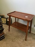 Full view angle of solid wood retro table with tapered legs and lower shelf on carpeted floor