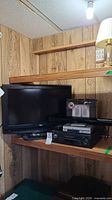 26-inch RCA TV along with Sharp VCR, Coby DVD player, and soundbar stacked on shelves against wood paneling