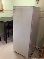Front and side view of white upright freezer with closed door, showing dimensions and a plugged-in power cord.