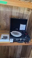 Vintage Innovative Technology 3-speed turntable inside open suitcase-style case with white platter, tonearm, control knobs, and power cord. Manual placed next to it.
