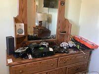 Wide view of Xbox console, controllers, headphones, various cables, and boxed items on a wooden dresser with mirror