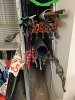 Photo of multiple metal bar clamps with orange, red, and gray handles, and a black metal pipe beneath them.
