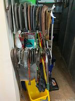 Wide view of the hanging clamps and pry bars showing a variety of metal clamps on wall-mounted rack along with long pry bars and tools.