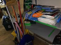 Full lot showing brooms, plastic bucket, green brush, extension poles, mop pads, and cleaning mitts.