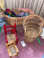 Photo showing wicker doll carriage filled with colorful hand knitted animals, red wooden rocking chair, and rattan fan chair.