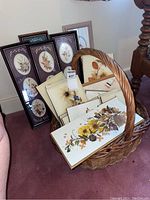 Assortment of framed botanical plaques in a large woven basket and leaning against wall