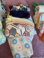 Five handmade blankets stacked: colorful crocheted hexagon patterned blanket on bottom, geometric hexagonal pattern blanket, pastel striped blankets with fringes, and patchwork knit blanket on top