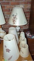 Image showing the white table lamp with Dornbush floral lamp shade and multiple loose lamp shades with botanical and leaf patterns, all vintage style with scalloped edges.