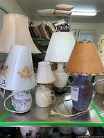 Four lamps on metal surface showing shades and bases, cords untangled and visible. Illumination off.