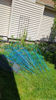 Multiple blue metal cone-shaped plant supports stacked on grass near siding of house