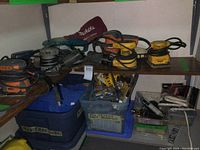 Multiple corded sanders on shelf with bins of accessories beneath