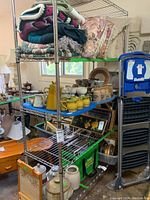 Photo of the metal wire shelving unit holding blankets, ceramic pitchers, jugs, bowls, and other household items.