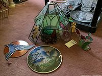 Green stained glass terrarium and various stained glass sun catchers including a cat with flower design, placed on carpet near glassware