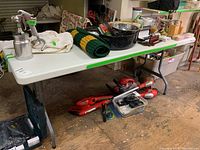 Long white molded plastic table with gray foldable metal legs, displaying miscellaneous items on top and underneath.