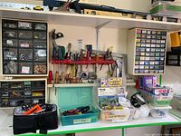 Tools and safety equipment organized on shelf and table. Visible screwdrivers, pliers, hardware kits, safety eyewear, first aid supplies and masks.