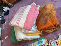 Lot of four wool blankets arranged on carpet; pink-striped Scottish wool blanket on top, rust-colored mohair blanket to the right, green and beige floral blankets below.