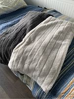Photo of two ribbed textured blankets folded side by side on a bed, one light grey and one dark grey.