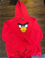 Red Angry Birds zip-up hoodie with front graphic of the red bird face and hood, laid flat on table.
