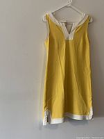 Photo of a yellow sleeveless Banana Republic dress with white trim on neckline and hem, hanging on a white hanger against a plain wall.