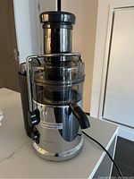 Front view of the centrifugal juicer showing the stainless steel base, feeding chute, and juice spout with power cord.