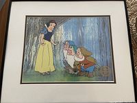 Frontal view of the framed limited edition sericel artwork depicting Snow White and two dwarfs on a forest background with black frame and cream matting.