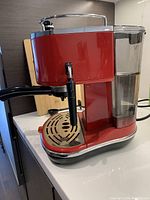 Side angle view showing the red DeLonghi espresso machine with water reservoir and steam wand.