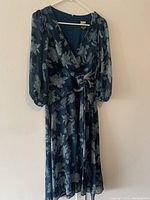 Photo of a blue floral pattern DKNY dress hanging, showing front view, semi-sheer long sleeves, V-neck and wrap style bodice.