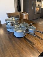 Masterchef cookware set with pots, pans and steamer on wooden table, shows non-stick grey coating and glass lids
