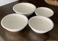 Four white ceramic bowls arranged on table showing varying sizes and shapes.