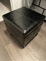 Black faux leather square ottoman with stitched cross detail on top.