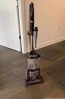 Photo of the Shark Navigator Swivel Upright Vacuum standing on hardwood floor showing its upright design and clear dust container.