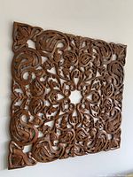 Front view of intricately carved square wooden panel hung on a white wall