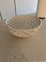 White ceramic woven lattice fruit basket on countertop, showing basket shape and open weave design.