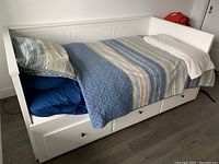 Side view of white wooden daybed with beadboard back, striped bedding, and three under-bed drawers