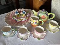 Wide view of entire Bombay Co. tea set including teapot, creamer, cups, saucers, and plates on white tablecloth