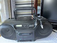 Front view of the GE boombox showing the closed CD player lid, dual front speakers, control buttons, and power cord coiled on top.