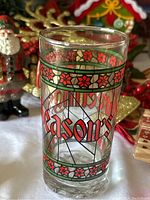 Close-up image of a vintage Christmas-themed glass decorated with red poinsettias and green leaves, displaying the text 'Season's Greetings.'
