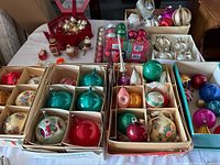 Top-down view of multiple boxes with various Christmas ornaments, mainly glass balls in multiple colors including red, green, gold, and hand-painted ones.