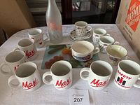 Full lot showing the mugs, coffee cups and saucers, the glass cutting board, and the frosted glass bottle with floral design.