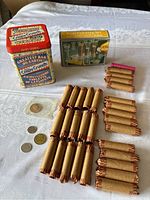 Coin counter set with coin sorter box, 30 rolls of pennies, two collectible tins, and loose coins arranged on table
