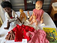 Vintage dolls arranged on a white tablecloth with accompanying children's clothing items.